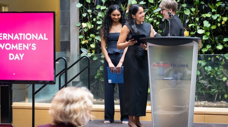 Someone receiving an award on stage from someone else while an individual behind smiles and watches